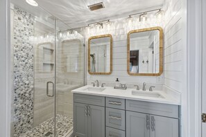 Ein Badezimmer mit einer gläsernen Dusche, zwei Waschbecken und einem Waschtisch mit Schubladen.