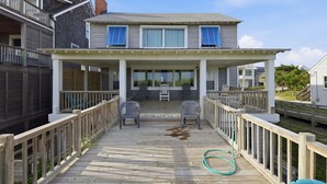 Une maison à deux étages avec un porche couvert, deux chaises et un tuyau d’arrosage sur la terrasse.