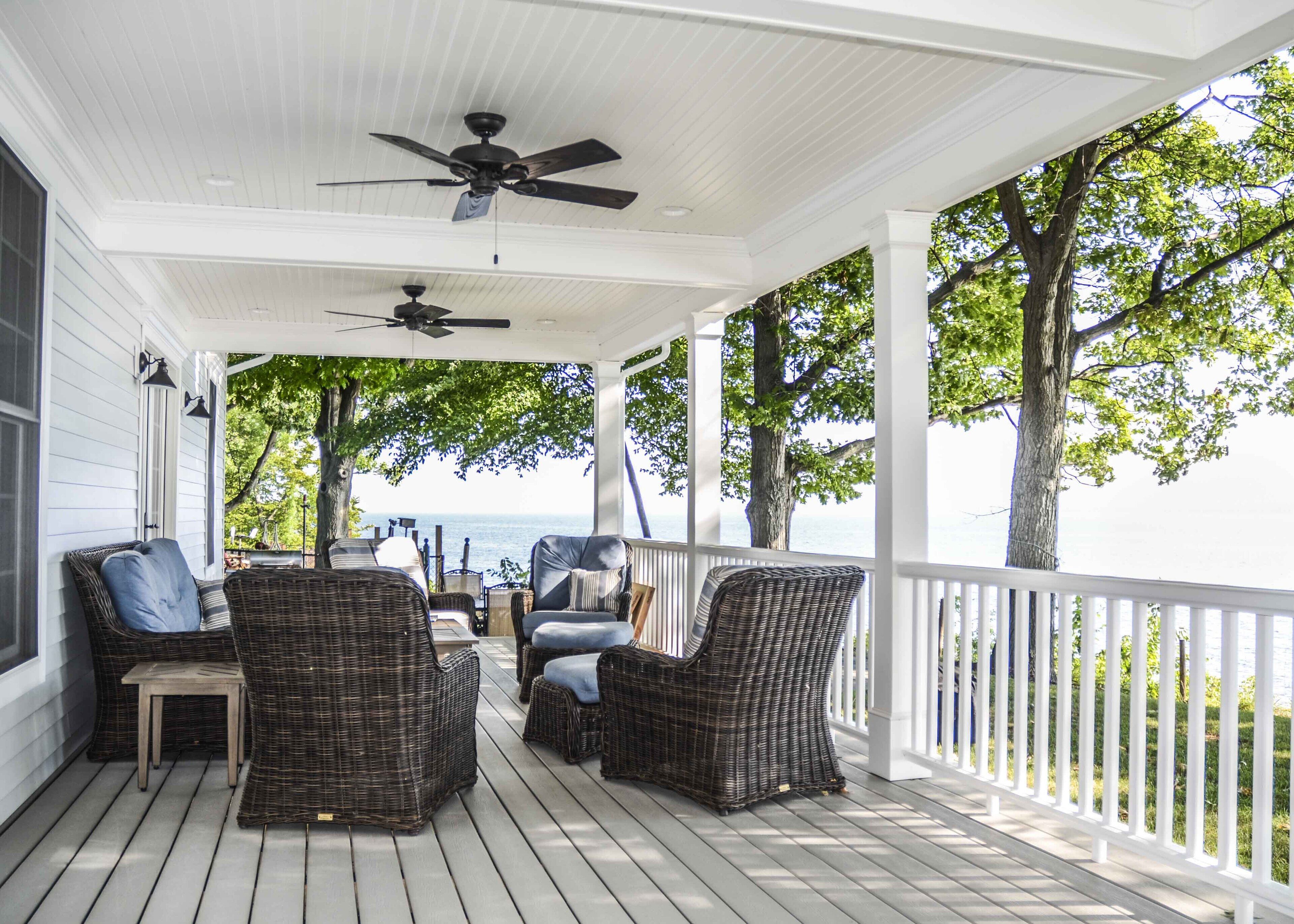 A covered porch with wicker furniture and ceiling fans, overlooking a body of water.