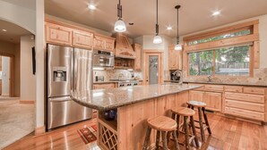 A kitchen with wooden cabinets, stainless steel appliances, a granite countertop, and bar stools. - Olive 4 BR Private Hot Tub, Fenced Yard, Pet-Friendly, Walk to Lake (Carnelian Bay)