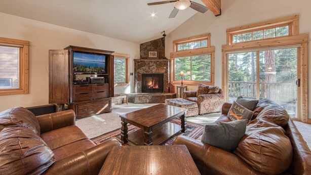 A spacious living room with leather furniture, a stone fireplace, and large windows. - Olive 4 BR Private Hot Tub, Fenced Yard, Pet-Friendly, Walk to Lake (Carnelian Bay)