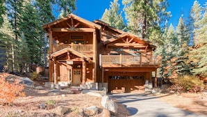 A two-story log cabin with a balcony, a garage, and a stone foundation. - Olive 4 BR Private Hot Tub, Fenced Yard, Pet-Friendly, Walk to Lake (Carnelian Bay)