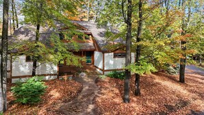 Eine rustikale Holzhütte mit steinernen Fundamenten, Holzbalken und einem steilen Satteldach, umgeben von einem Wald im Herbstlaub.
