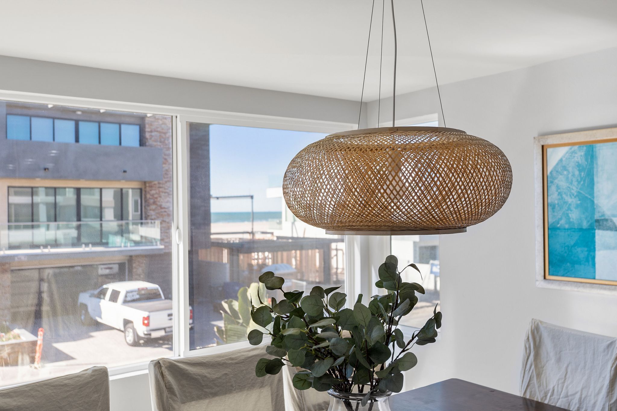 A modern interior with a large window, a wicker pendant light, and a potted plant.