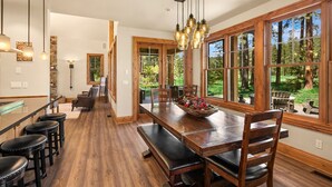 A spacious kitchen with wooden flooring, a long dining table with benches, and large windows offering a view of the outdoors. - Must See Suncadia Retreat! 3 Masters * Hot Tub * Game Room * On the Course! (Cle Elum)