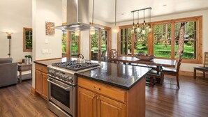A spacious kitchen with a large island, wooden cabinets, and a view of a lush garden through large windows. - Must See Suncadia Retreat! 3 Masters * Hot Tub * Game Room * On the Course! (Cle Elum)