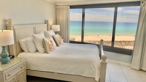 Un dormitorio con cama, mesitas de noche y vista a la playa.
