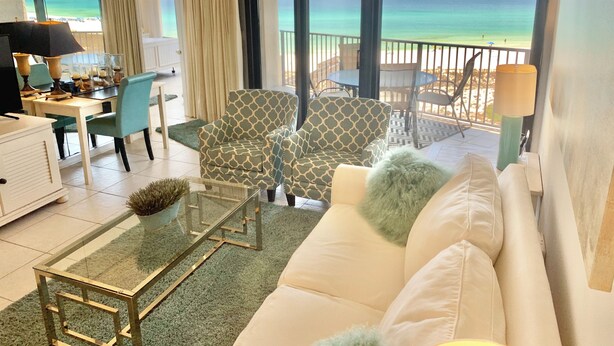 Amplia sala de estar con un gran ventanal con vista a la playa, un comedor con mesa y sillas, y una zona de estar acogedora con un sofá y sillones.