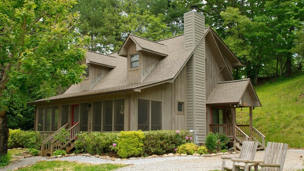 A wooden cabin with a sloped roof, a front porch, and a gravel driveway.
