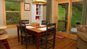 A dining area with a wooden table and chairs, a chandelier, and a view of greenery through a window.
