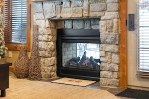 A stone fireplace with a black frame, two decorative woven vases, and a mat on the floor.