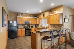 A kitchen with wooden cabinets, a black refrigerator, a microwave, and a stove. There is a sign on the wall that says "Winter Wonderland."