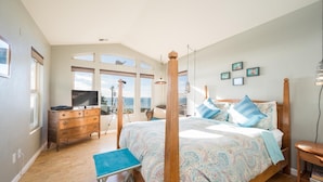 Une chambre à coucher avec un lit à baldaquin, une commode en bois, un petit banc bleu et un téléviseur posé sur une autre commode.