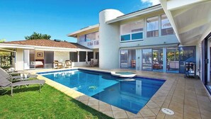 Ett modernt hus med en swimmingpool, utomhusmöbler och en täckt uteplats.