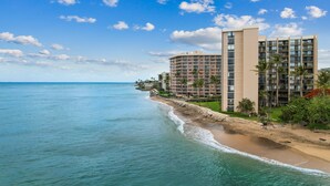 Ein Strandhotel mit mehreren Etagen, einem sandigen Strand und wolkenlosem, blauem Himmel.