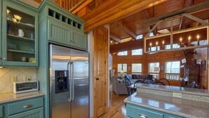 A modern kitchen with a stainless steel refrigerator, teal cabinetry, and a granite countertop. - Chipmunk Chase in Gated Smoky Mountain Retreat Community (MAGGIE VALLEY)