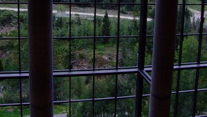 A view through a window with a grid pattern, displaying a mountainous landscape with greenery and a river. - Prime Ski Week at Snowbird's Cliff Club Sleeps 6 in 1bedroom (Sandy)
