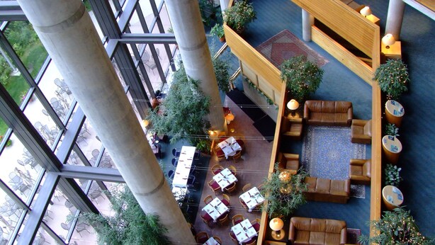 A spacious atrium with multiple levels, featuring a central seating area with sofas and tables, surrounded by potted plants and a patterned carpet. - Prime Ski Week at Snowbird's Cliff Club Sleeps 6 in 1bedroom (Sandy)