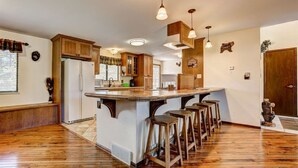 A kitchen with wooden cabinets, a central island with stools, pendant lighting, and a refrigerator.