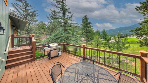 A wooden deck with a grill, outdoor seating, and a view of a mountainous landscape.