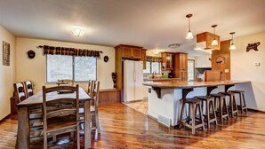 A spacious kitchen with wooden flooring, a central island with stools, and a dining area with a wooden table and chairs.