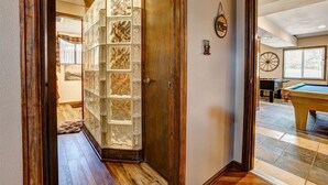 A hallway with a wooden door, a glass partition, and a pool table in the adjacent room.