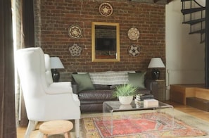 A cozy living room with a brick wall, a sofa, a white armchair, a coffee table, and decorative plates.