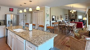 A spacious kitchen with granite countertops, a central island, and a dining area with a red sofa and wicker chairs. - Lakefront Rumbling Bald Retreat, HotTub, Kayaks, SUP's, Floating Dock (Lake Lure)