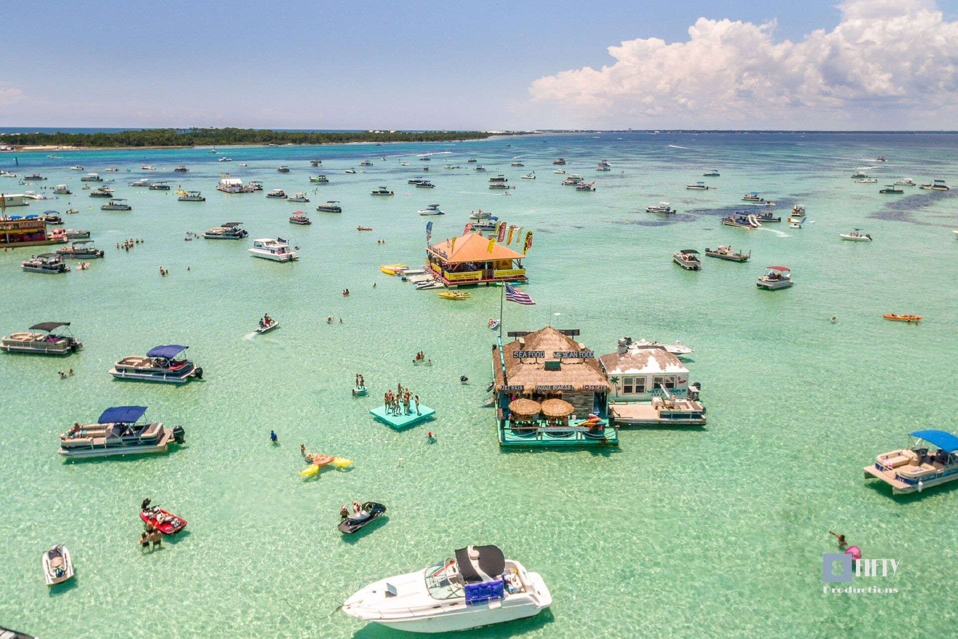 A marina with numerous boats and a few small buildings with signs indicating seafood and Mexican food.