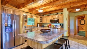 A kitchen with wooden cabinets, stainless steel appliances, a granite countertop, and a large island with a bowl and flowers.