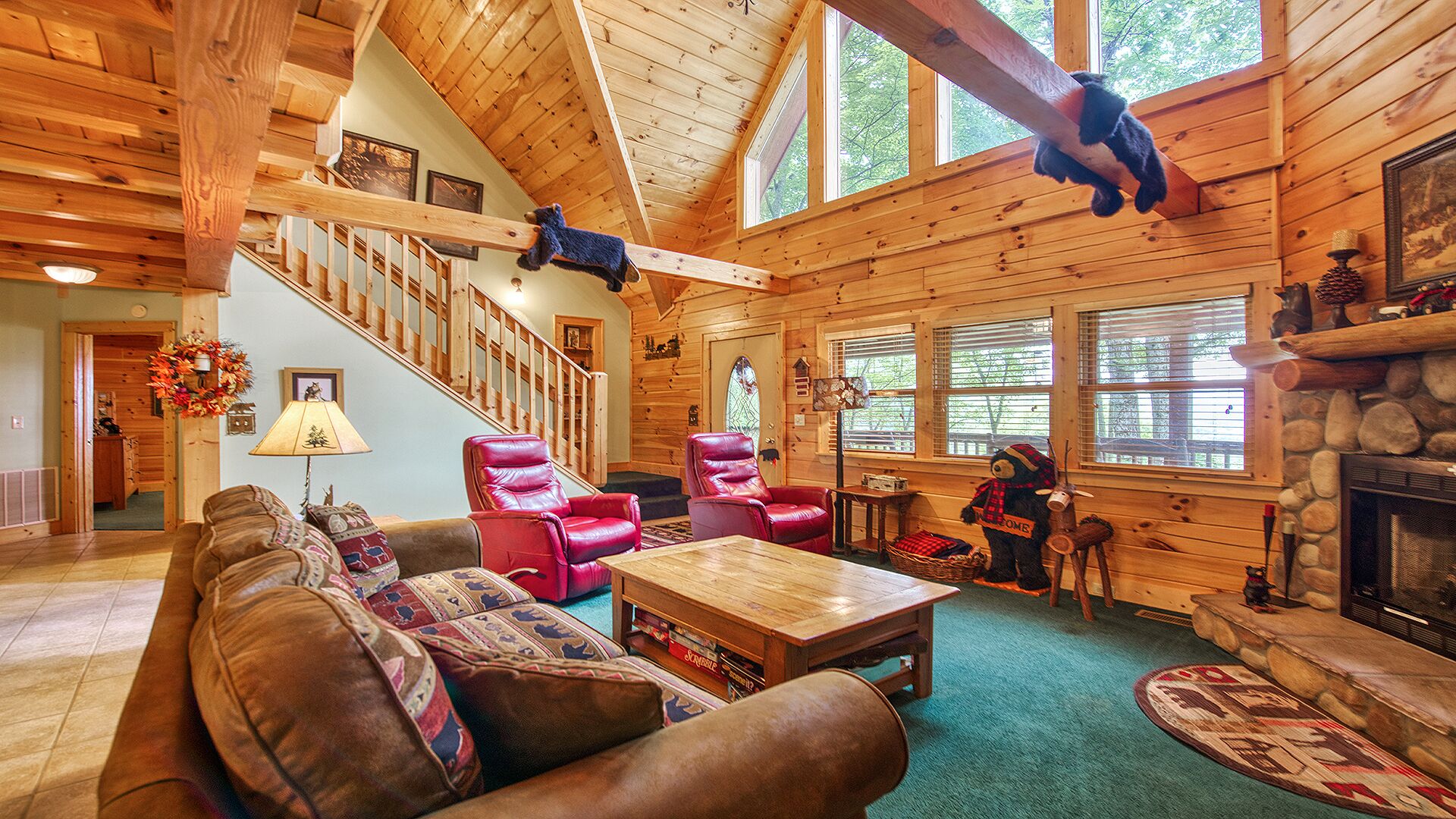 A log cabin interior with a wooden staircase, leather chairs, a fireplace, and a bear decoration.