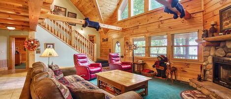 A log cabin interior with a wooden staircase, leather chairs, a fireplace, and a bear decoration.