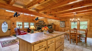 A spacious log cabin interior with a large kitchen island, dining area, and a cozy living room.