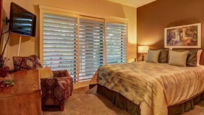 Un dormitorio con cama, televisión, escritorio y ventana con persianas.