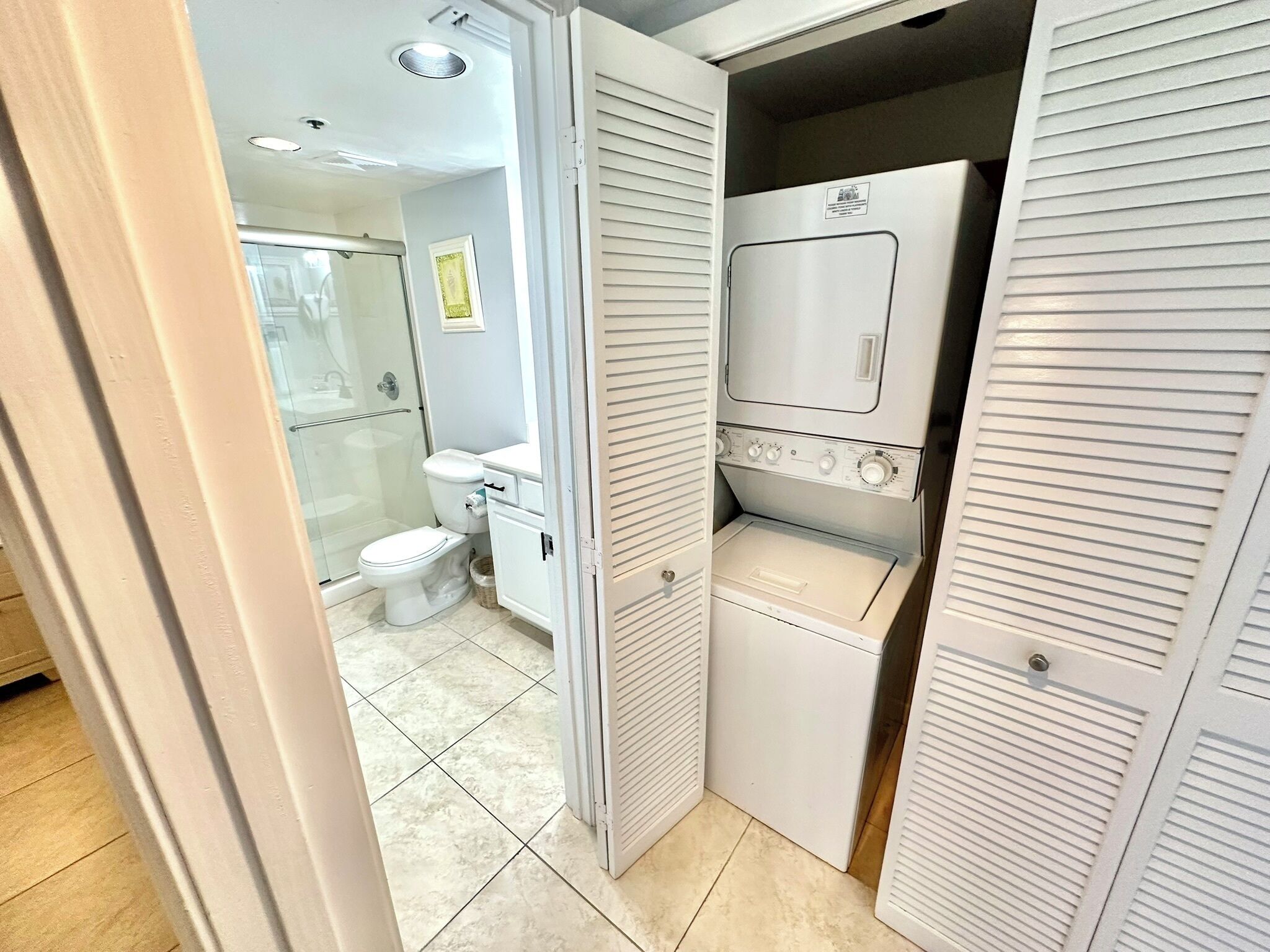 Une salle de bain compacte comprenant des toilettes, une douche et un appareil combiné lave-linge et sèche-linge intégré.