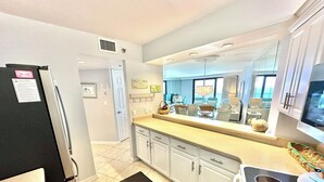 A modern kitchen with white cabinets, a black refrigerator, and a large window offering a view of the living area. - Fabulous gulf/beach views from the 14th floor! 4336BS2 (Miramar Beach)