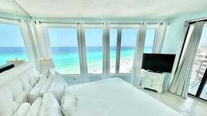 A large bed with white bedding, a television on a dresser, and a view of the beach and ocean through large windows. - Dazzling Beach View 6 Seat Golf Cart included! 4321 BS2 (Miramar Beach)
