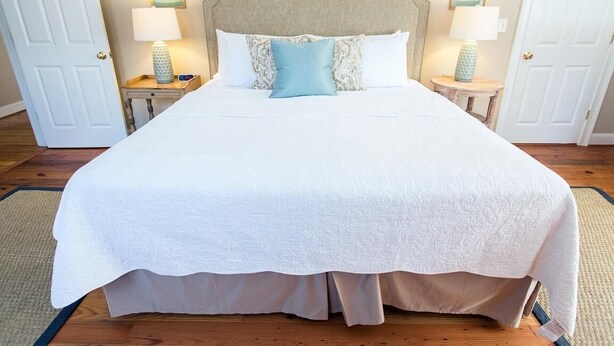 A large bed with a white bedspread and a decorative headboard. There are two bedside tables with lamps and decorative items.