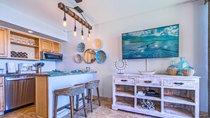 Una cocina con una isla central, taburetes de bar, un microondas y un accesorio de iluminación decorativo.