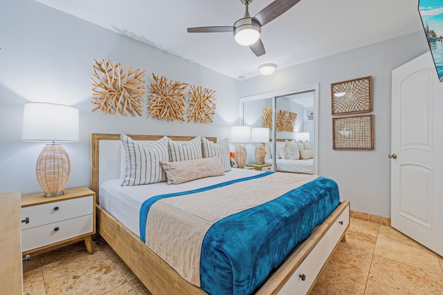 A bedroom with a bed, bedside tables, a ceiling fan, wall art, and a door.