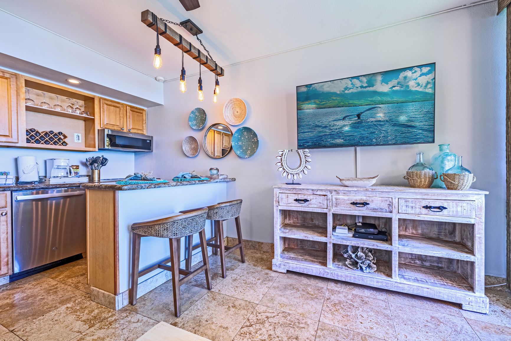 A kitchen with a central island, bar stools, a microwave, and a decorative light fixture.