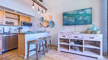 A kitchen with a central island, bar stools, a microwave, and a decorative light fixture.