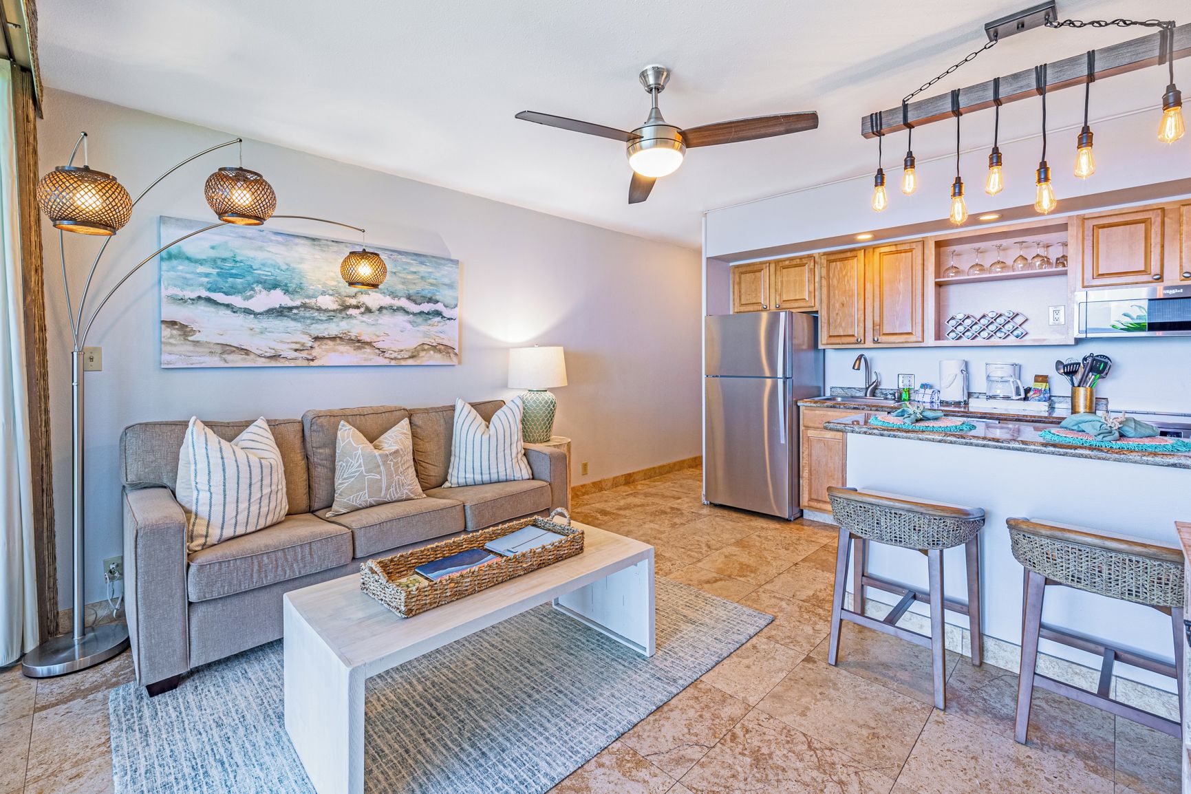 A modern living room with a grey sofa, a coffee table, and a kitchen area with wooden cabinets and a refrigerator.