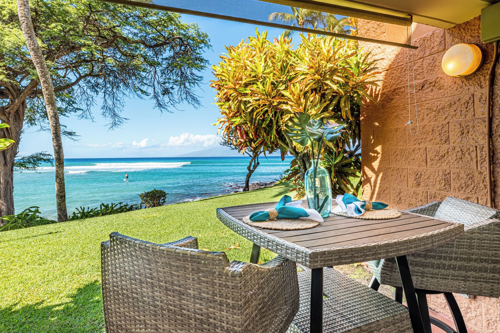 Eine Terrasse im Freien mit Korbmöbeln, einem Tisch mit einer Vase und Servietten sowie Blick auf den Ozean.