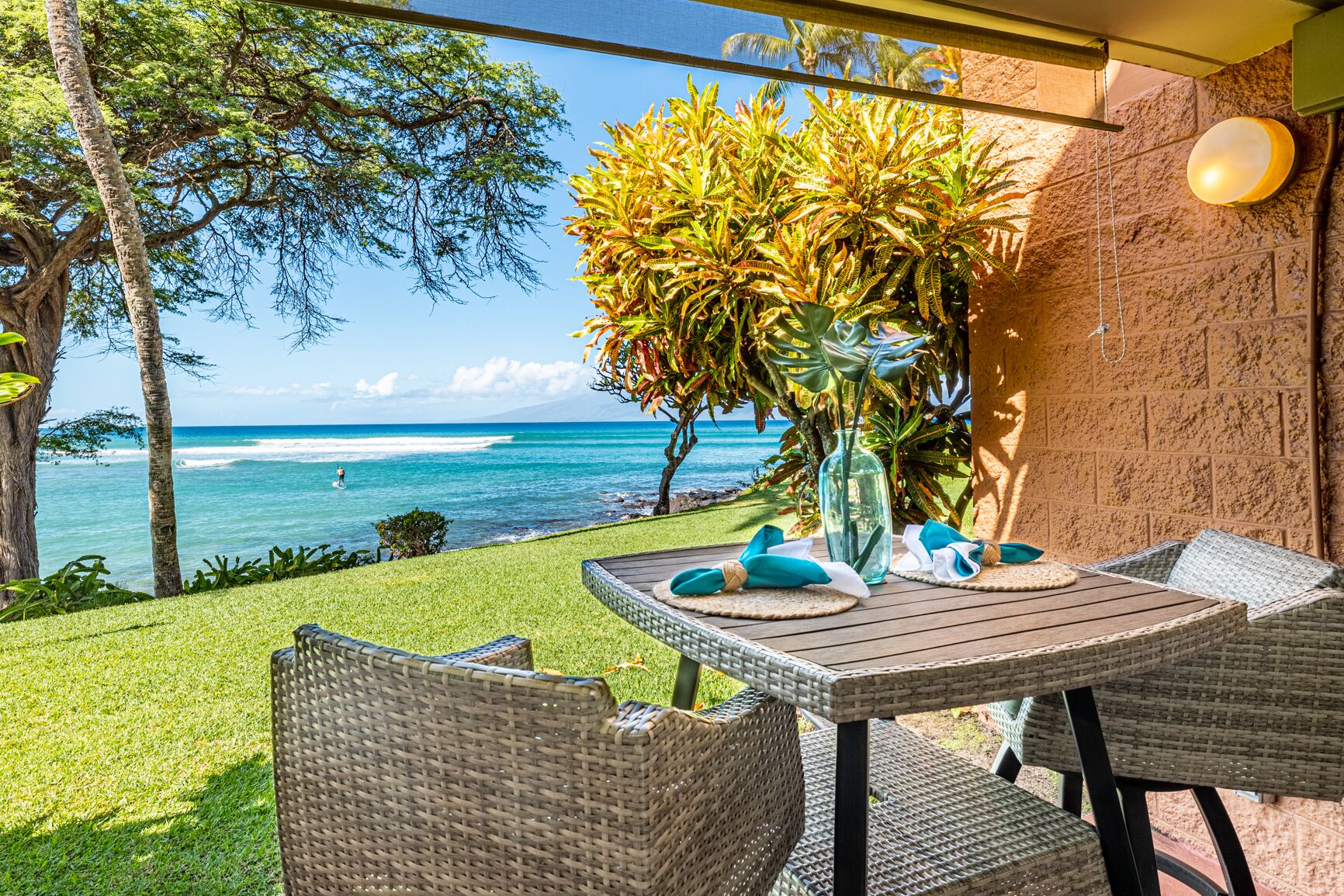 An outdoor patio with wicker furniture, a table with a vase and napkins, and a view of the ocean.