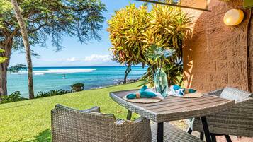 An outdoor patio with wicker furniture, a table with a vase and napkins, and a view of the ocean.