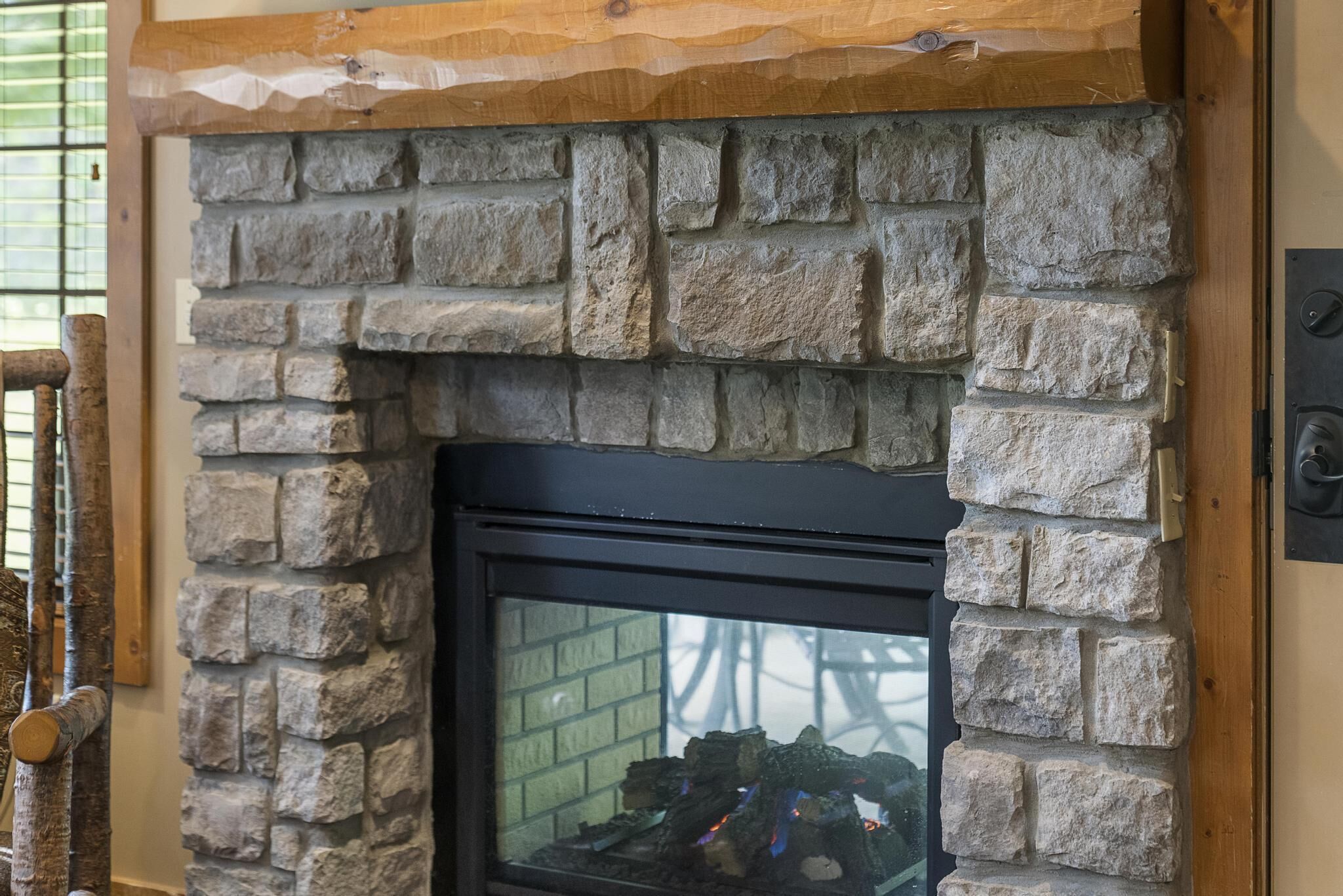 A stone fireplace with a black glass door, set in a wooden frame.