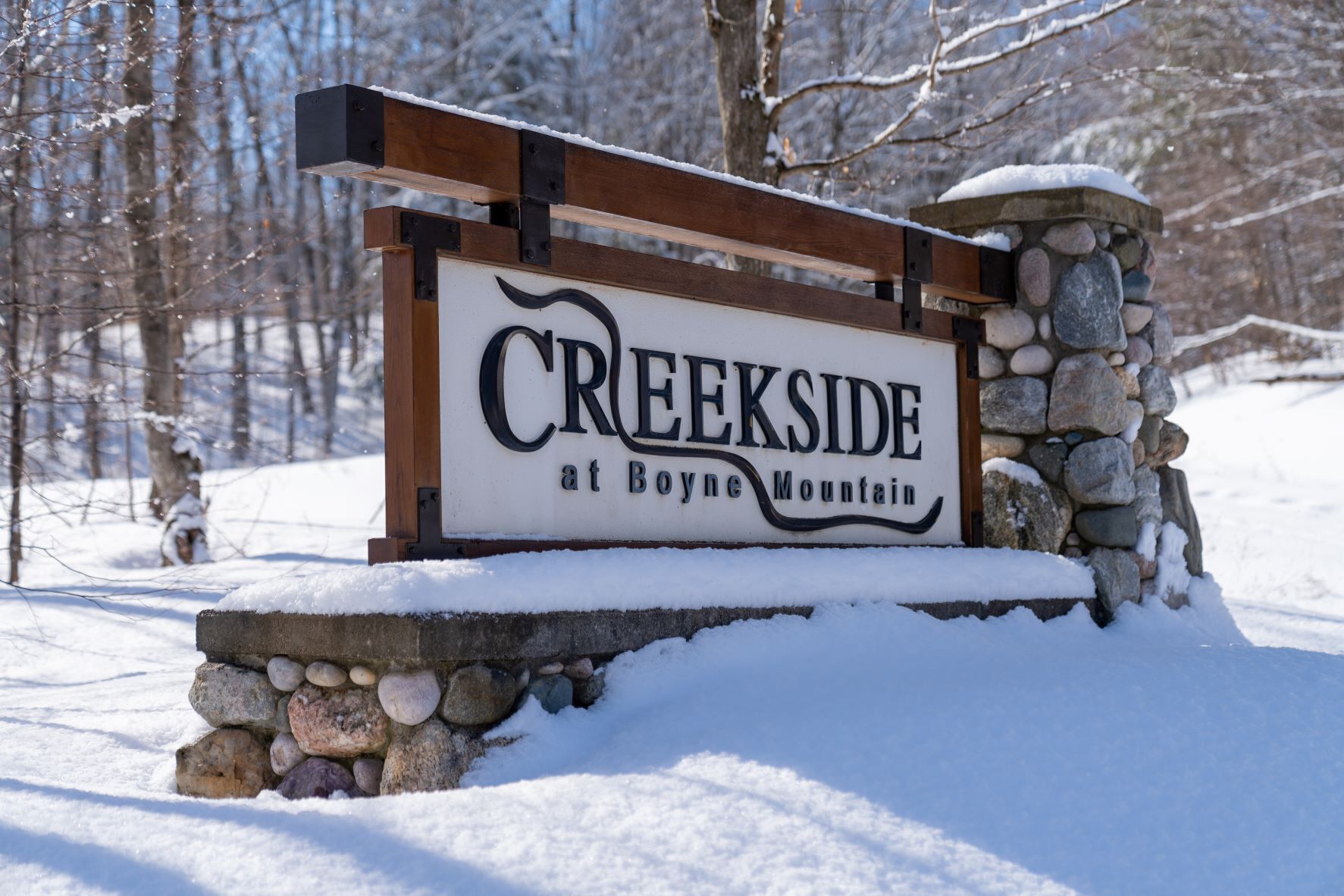 Een houten bord met de tekst 'CREEKSIDE at Boyne Mountain', omringd door een stenen muur en sneeuw.