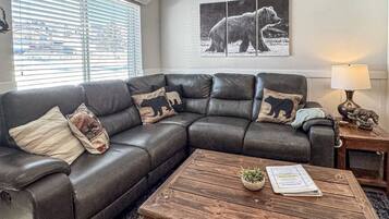 A living room with a leather sectional sofa, a wooden coffee table, and a bear-themed pillow.