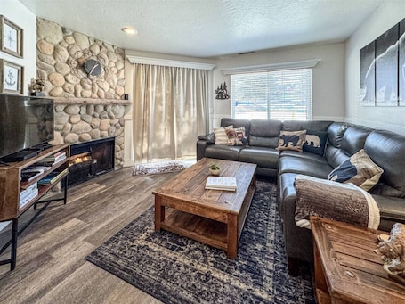 A living room with a stone fireplace, a leather sofa, a coffee table, and a television.